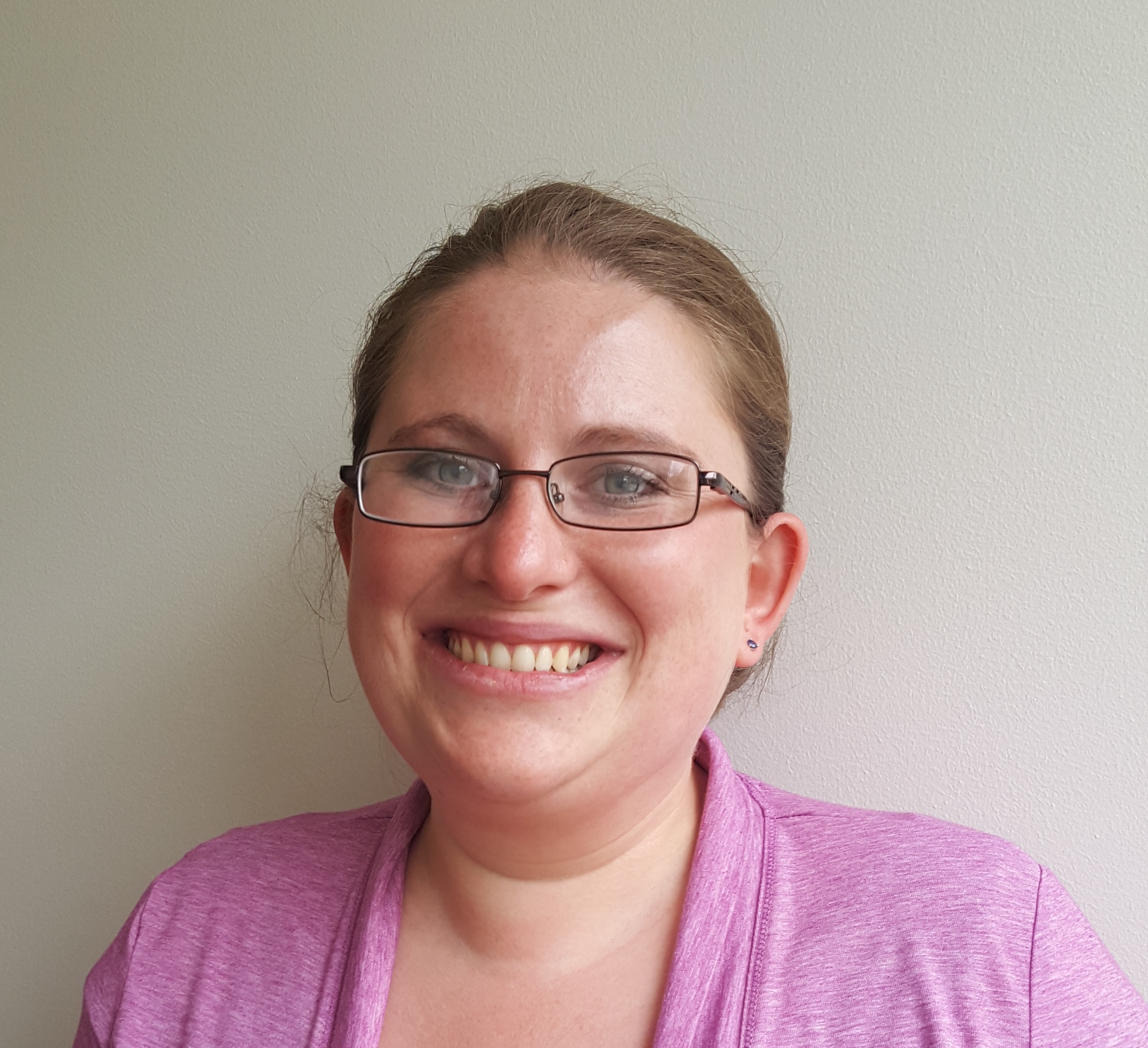 White woman with her hair pulled back wearing glasses and a pink shirt