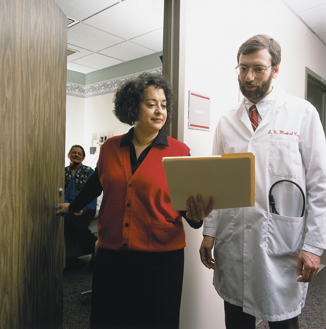 A Behavioral Health Care Manager leaves an exam room and shares a file with a doctors.